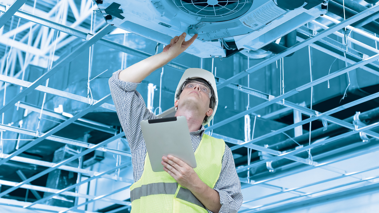 Homme en gilet pare-balles tenant un iPad et inspectant un système de chauffage, de ventilation et de climatisation (CVC)